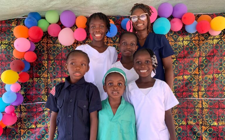 A group of smiling primary school students standing together on Occupation Day at Zoe Robinson Academy, displaying signs and dressing up for their future career aspirations.