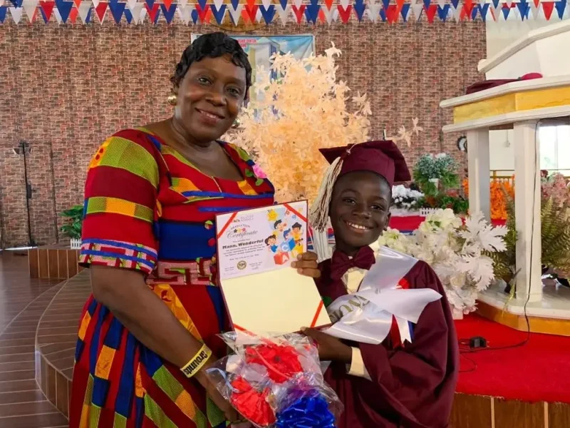 A Zoe Robinson Academy kindergarten graduate holding his certificate beside the Hilltop Schools social worker.